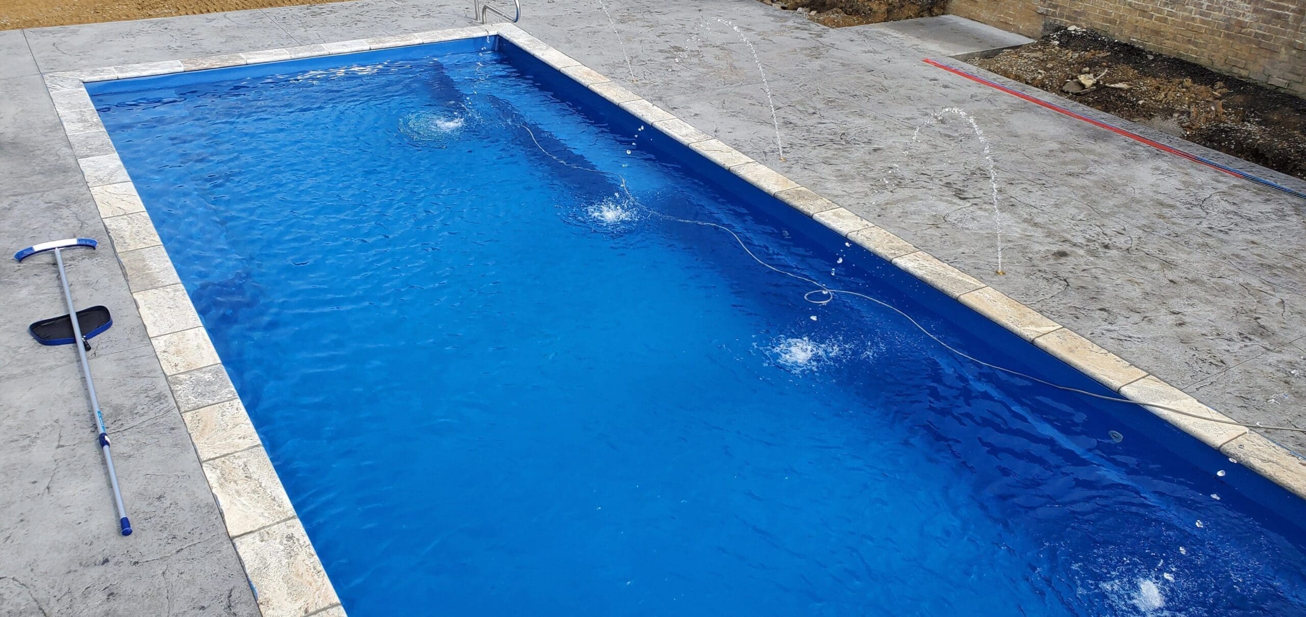 A rectangular swimming pool with blue water, surrounded by a concrete deck, with a pool skimmer resting on the side.