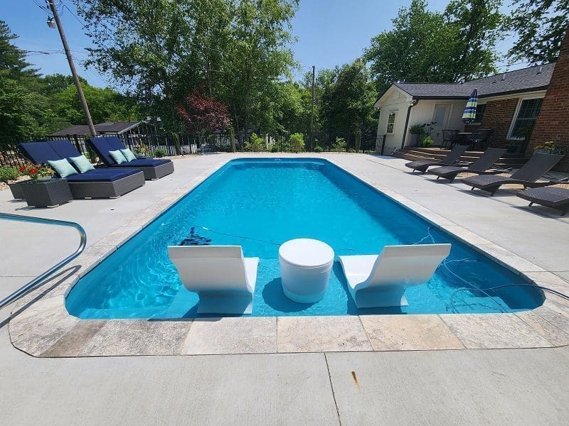 A backyard swimming pool with a lounge area on a sunny day.