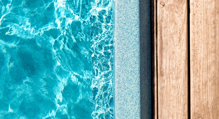 Swimming pool edge with clear blue water alongside a wooden deck, featuring a fiberglass pool installation guide.