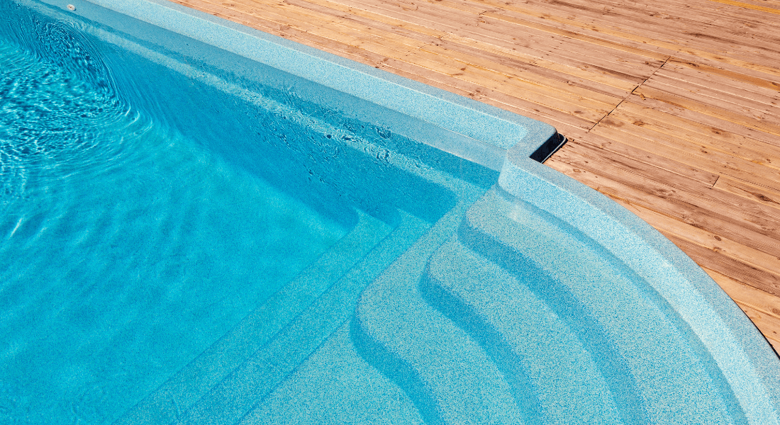 Top-down view of a corner of a swimming pool with clear blue water next to a wooden deck.