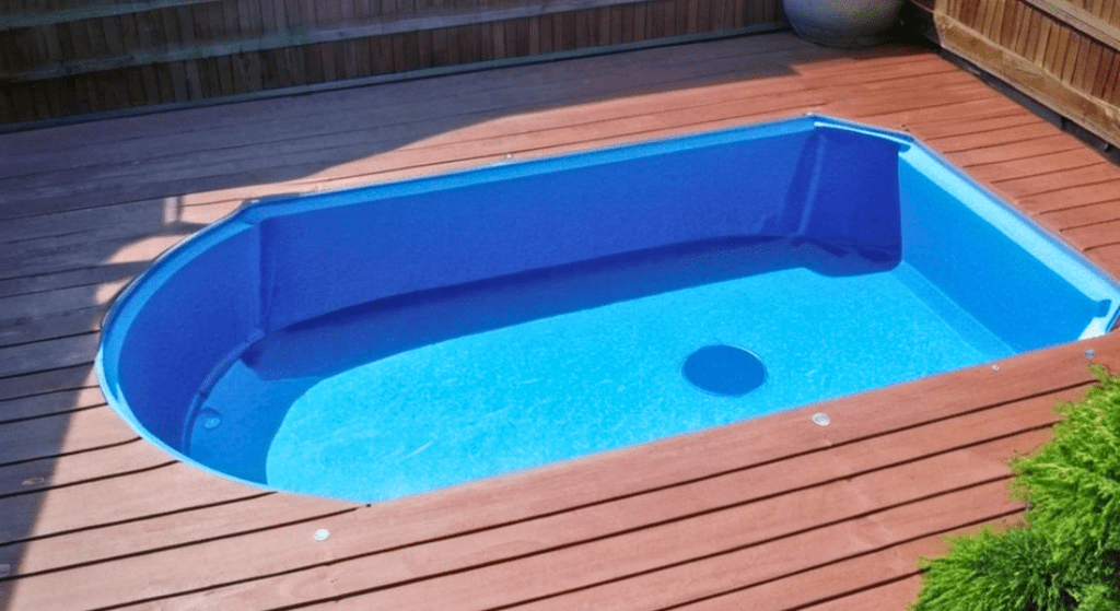 A small blue rectangular swimming pool with a rounded end is set into a wooden deck. Nearby greenery and a potted plant are visible.
