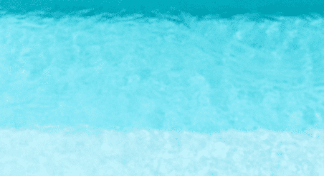 A top-down view of a clear, turquoise swimming pool. The different shades of blue suggest varying depths of water.