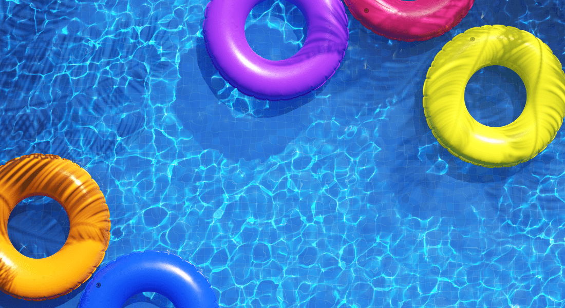 Five colorful inflatable swim rings (orange, purple, pink, yellow, and blue) float on the surface of a clear blue swimming pool.